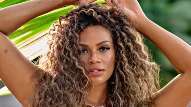 Kamie Crawford poses for the camera with her brown curly hair down and her arms raised above her head.